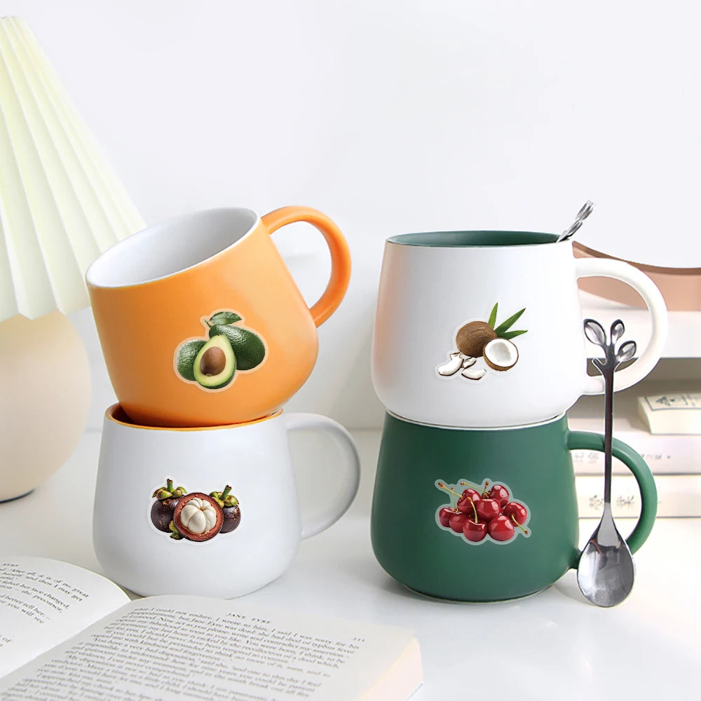 A set of three ceramic mugs in orange, white, and green featuring fruit designs are displayed on a white surface.