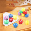 A set of five colorful gonggi stones in various shades of green, yellow, pink, and blue arranged on a wooden surface.