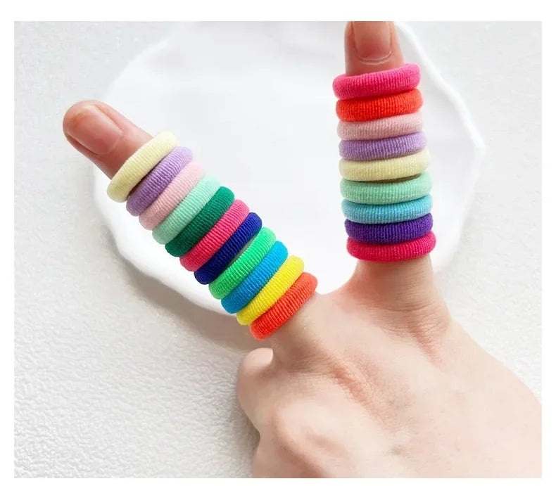 A hand displays a stack of colorful nylon hair ties in various shades of pink, purple, green, and yellow.