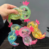 A hand holds a bright green and pink squishy axolotl stress relief toy with glittery skin.