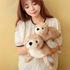 A woman is holding a brown seal plush toy with a white face and blue tag.