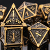 A close-up of a set of seven gold and black metal dice, including a prominent house-shaped die featuring a skull and dragon d
