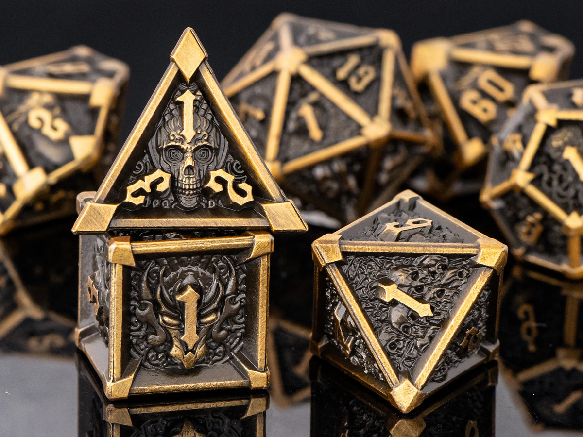 A close-up of a set of seven gold and black metal dice, including a prominent house-shaped die featuring a skull and dragon d