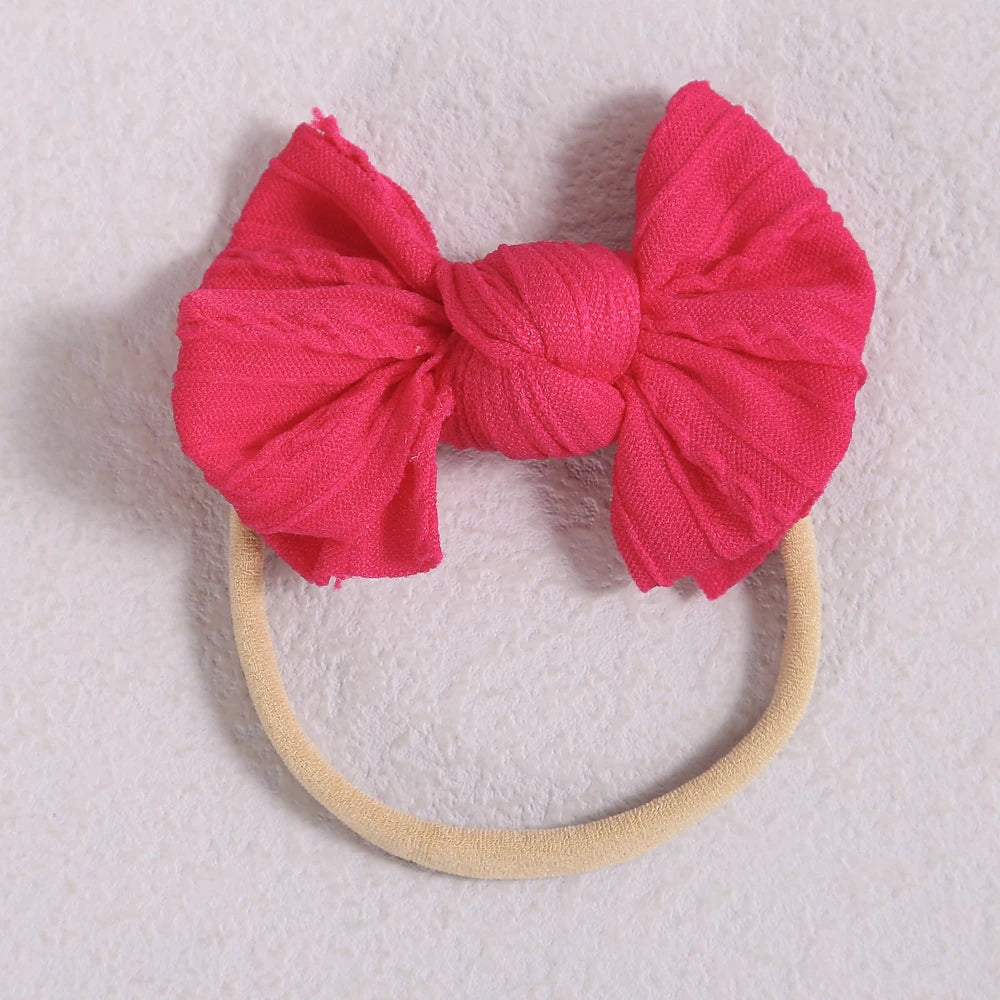 A bright pink fabric bow headband with a light beige elastic band, displayed on a white background.