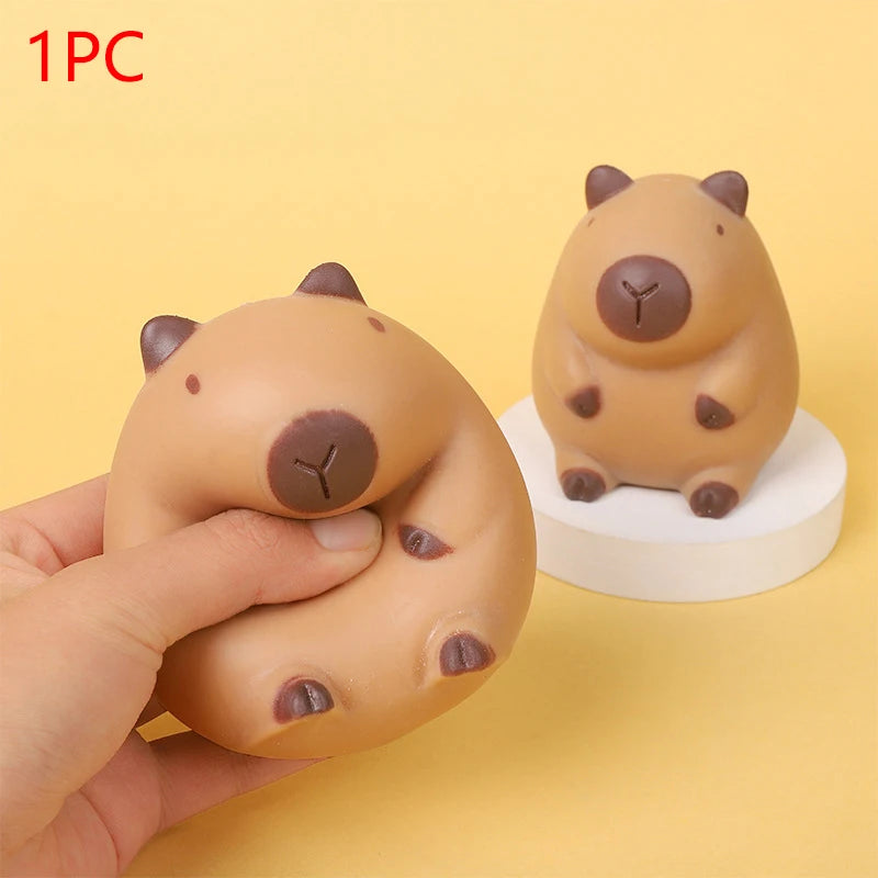 A light brown, squishy capybara stress relief toy is being held by a hand against a plain yellow background.