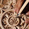 A hand uses a wood carving chisel to shape a detailed floral design in a wooden carving set.