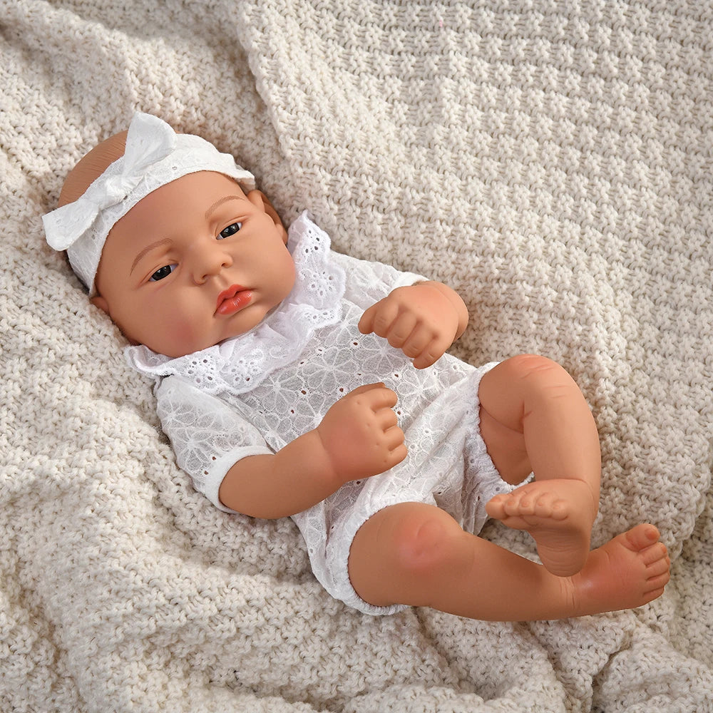 A lifelike vinyl reborn doll with a white outfit lying on a cream-colored knitted blanket.