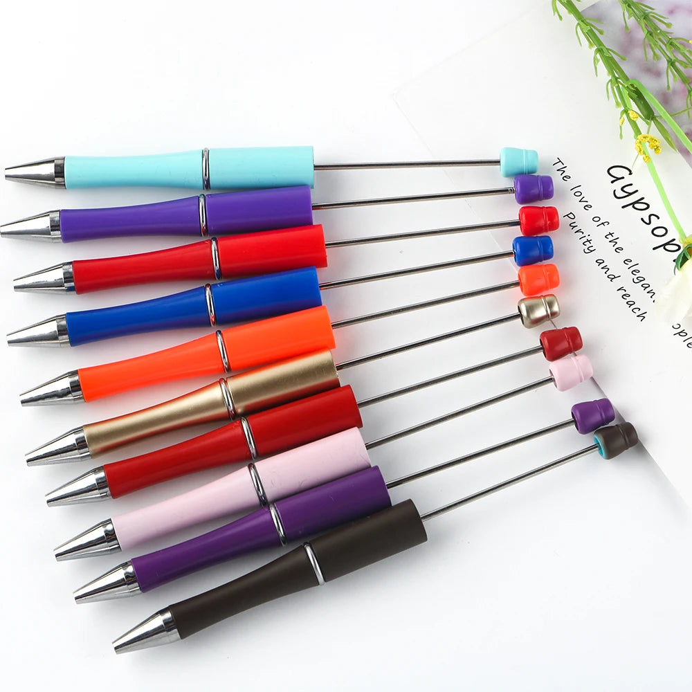 A collection of colorful beadable ballpoint pens arranged in a diagonal line on a white background.