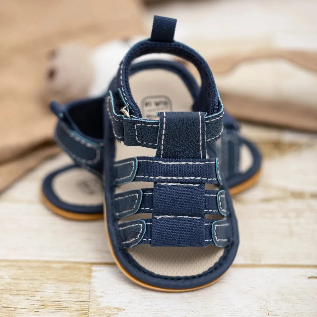 A pair of navy blue soft non-slip baby sandals for first walkers resting on a light wooden surface.