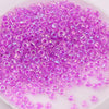 A pile of small, translucent purple glass rice beads for DIY jewelry and crafting.