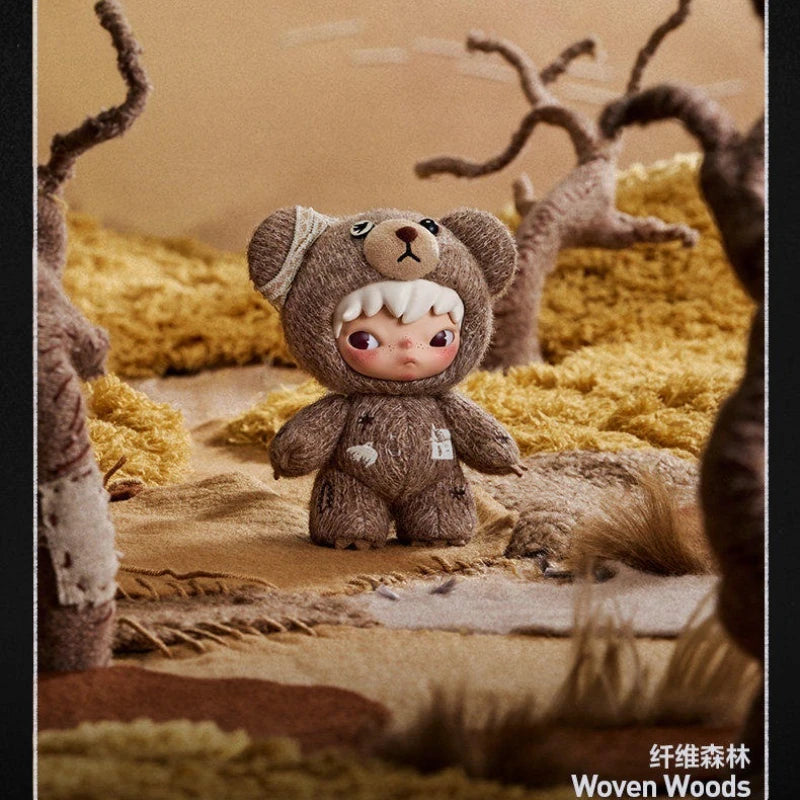 A small, brown teddy bear plush doll is positioned in a dry, golden landscape surrounded by textured natural elements.