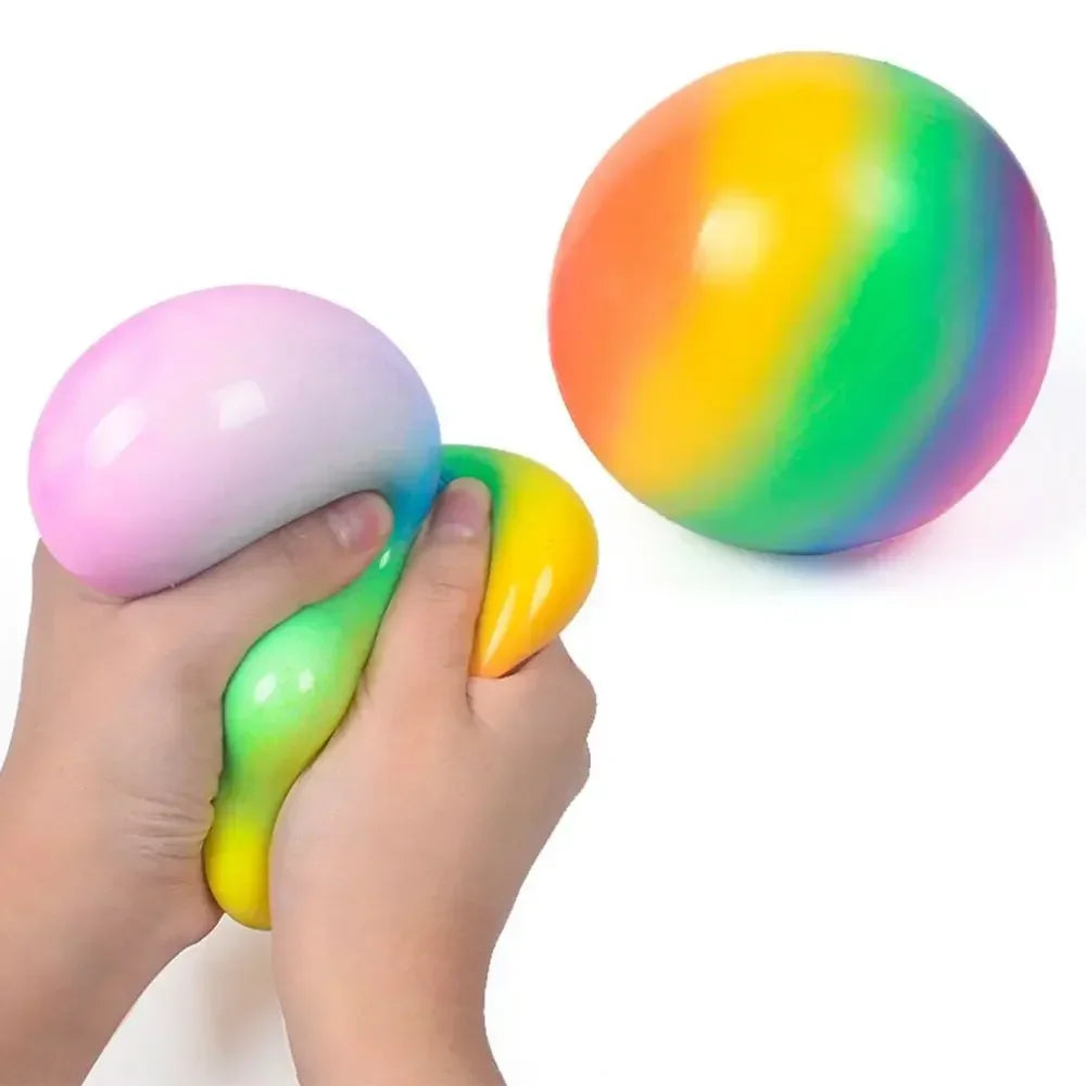 A hand is squeezing a colorful water bead stress ball with a bright rainbow gradient.