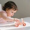 A baby is interacting with a pink silicone toy car set on a white surface.