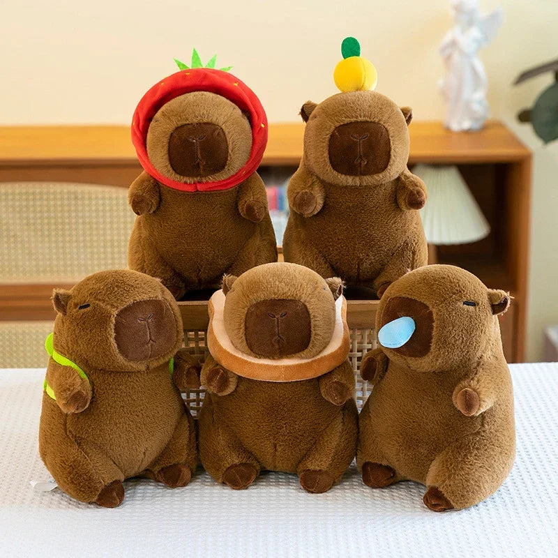 A set of three brown capybara plush toys with green accents sitting on a white surface.