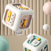 A white Montessori early education cube with colorful inserts and a yellow ball shown next to other spherical objects.