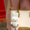 A white Miffy plush keychain charm with a bakery theme is attached to a tan leather handbag.