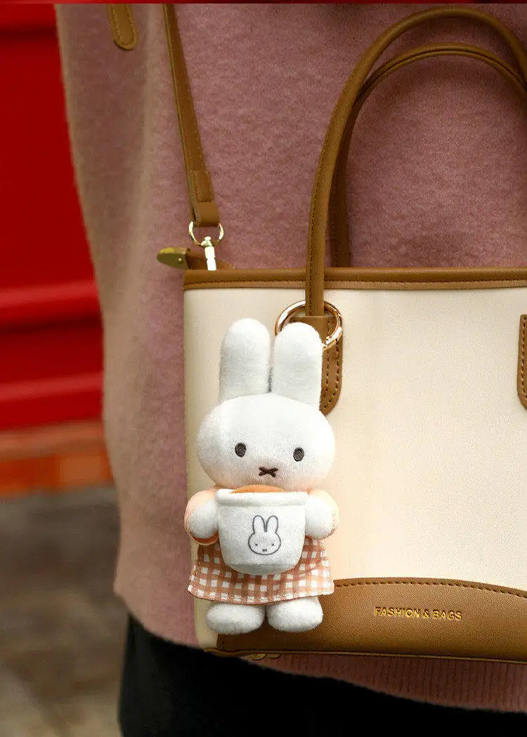 A white Miffy plush keychain charm with a bakery theme is attached to a tan leather handbag.