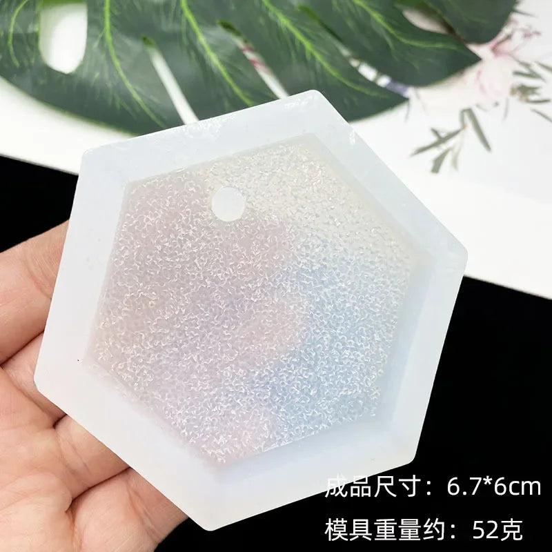 A clear silicone resin mold set with various geometric shapes is held in a hand against a blurred green leaf background.