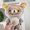 A hand is holding a soft gray Rilakkuma anime plush bear with yellow ears and a white chest.