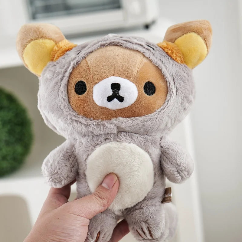 A hand is holding a soft gray Rilakkuma anime plush bear with yellow ears and a white chest.