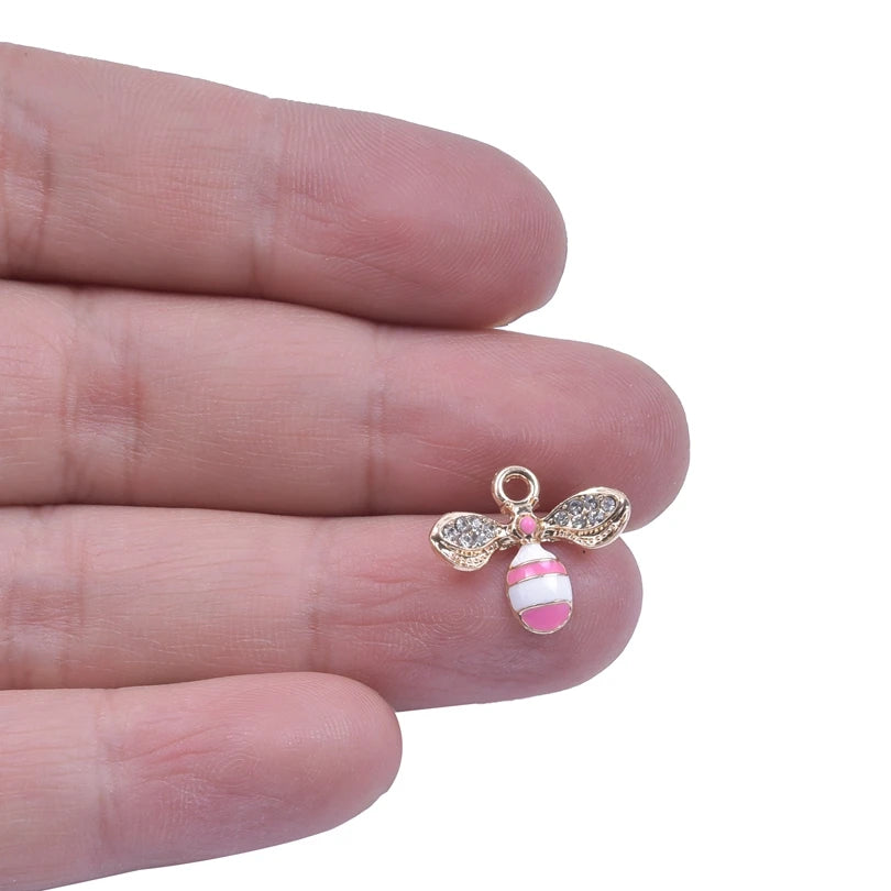 A hand holds a small, pink and white striped bee enamel charm for jewelry making.