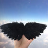 A hand holds a pair of black feather angel wings against a bright blue sky.