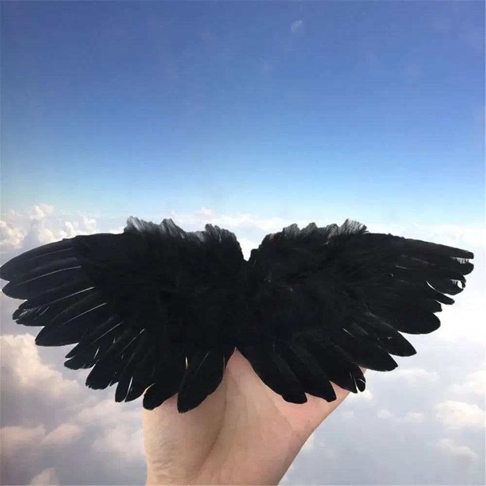 A hand holds a pair of black feather angel wings against a bright blue sky.