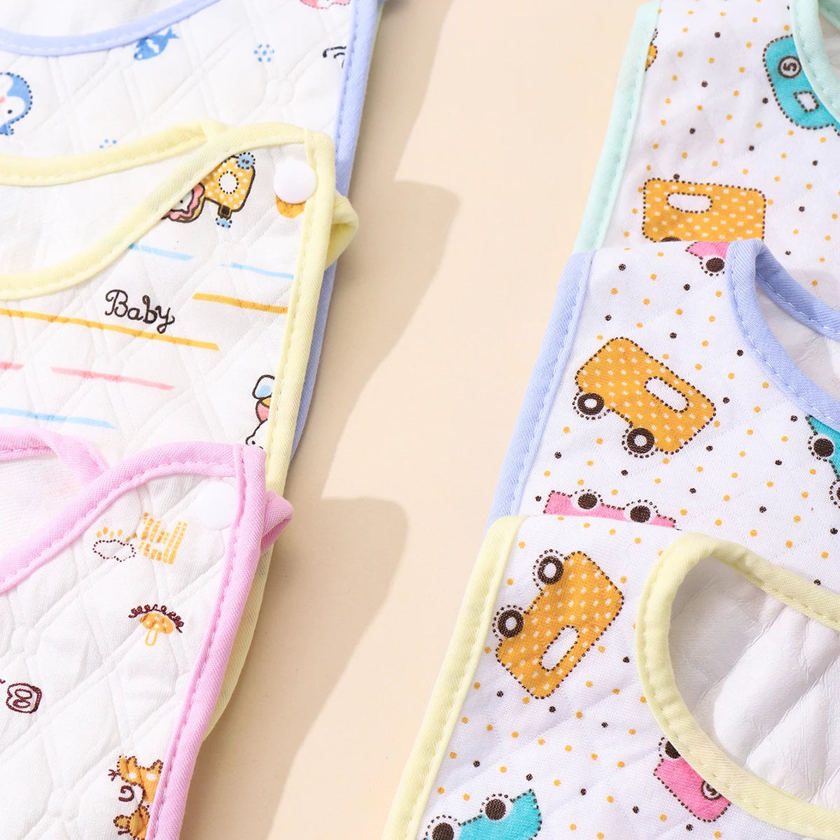A close-up of three soft cotton baby bibs with adjustable closures in pastel colors and patterns.