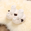 A pair of white, fluffy cartoon baby booties shaped like a sleeping animal resting on a cream-colored faux fur rug.