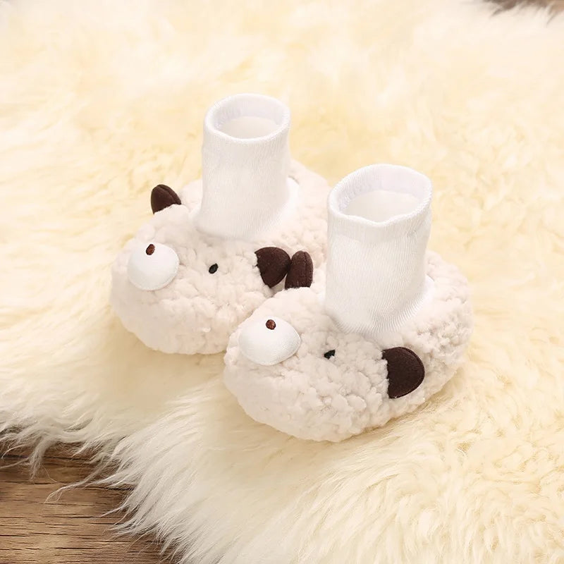 A pair of white, fluffy cartoon baby booties shaped like a sleeping animal resting on a cream-colored faux fur rug.