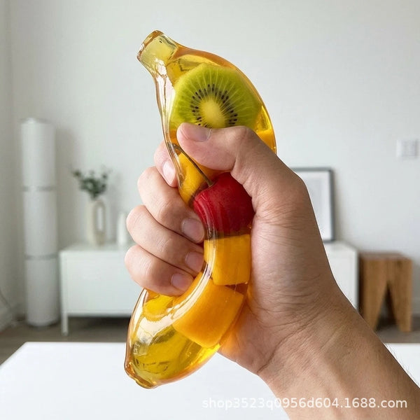 Une main tient un jouet squishy jaune en forme de fruit, ressemblant à un kiwi et une banane.