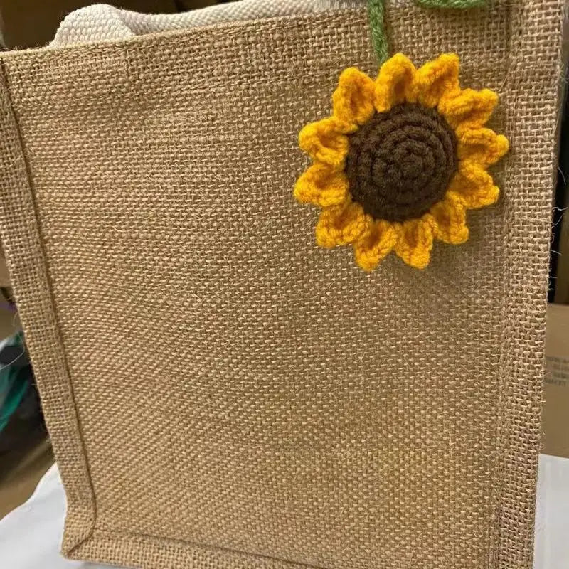 Handmade crochet sunflower charm attached to a beige woven fabric pouch.