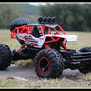 A red and black 4WD off-road monster truck with large tires and an LED headlight setup on a grassy field.