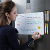 A woman writes a to do list on a magnetic dry erase board attached to a refrigerator.