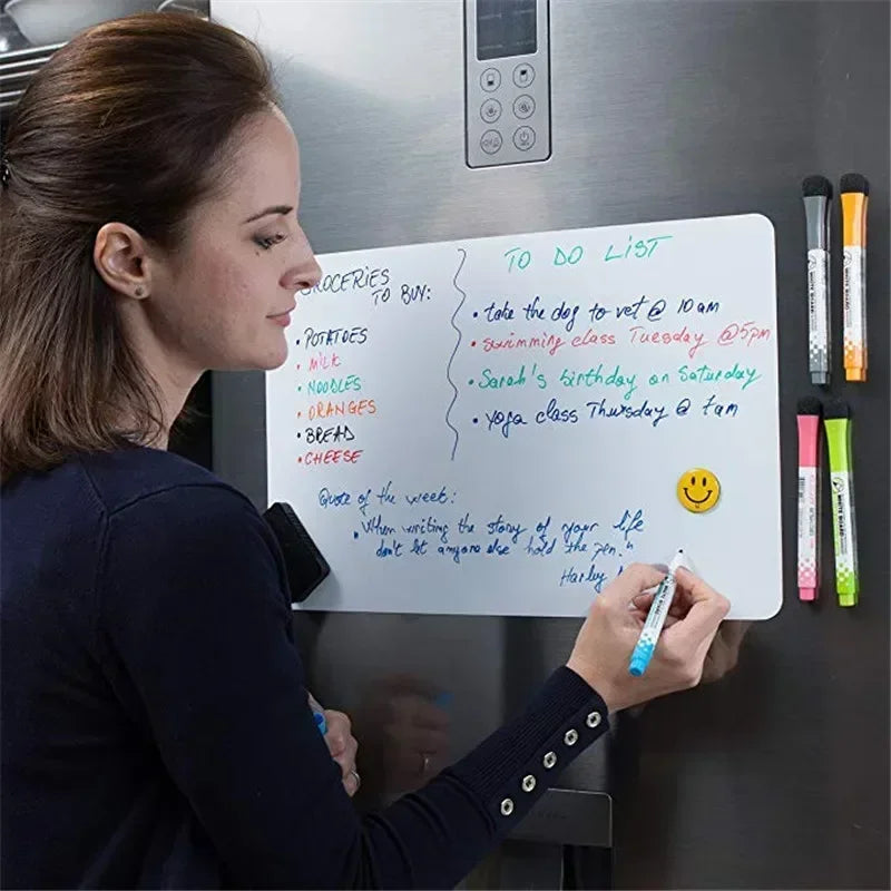 A woman writes a to do list on a magnetic dry erase board attached to a refrigerator.