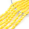 A strand of yellow heart-shaped acrylic beads for jewelry making laid out on a white surface.