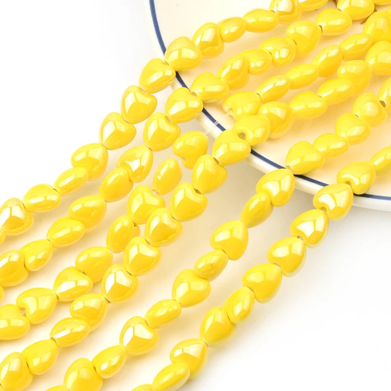 A strand of yellow heart-shaped acrylic beads for jewelry making laid out on a white surface.