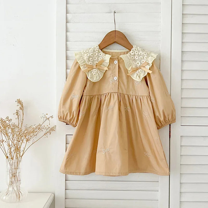 A light beige cotton party dress for girls featuring lace collar details and embroidered accents, displayed on a hanger.