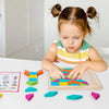 A young girl is assembling a wooden geometric shape puzzle with colorful blocks on a white table.