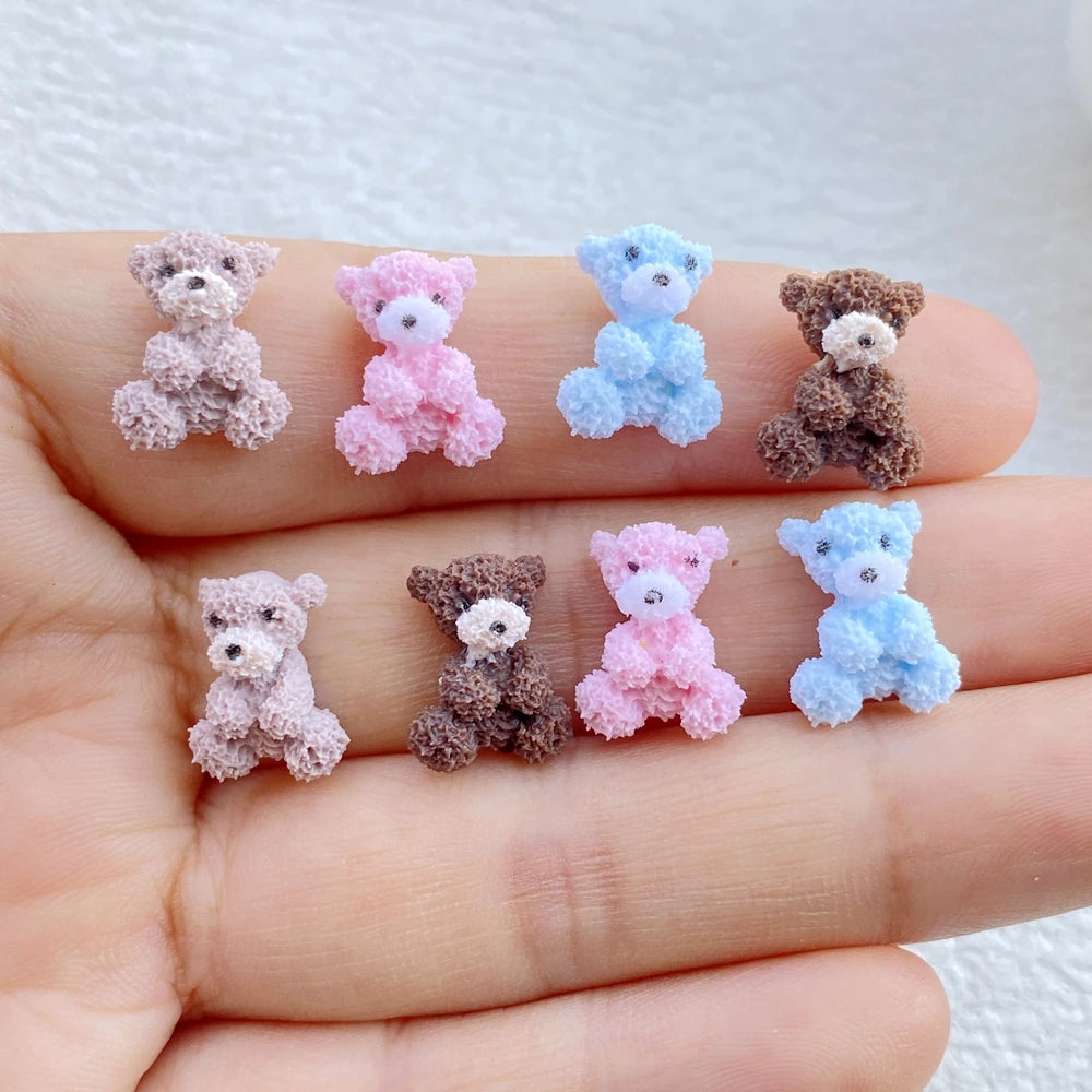 A hand displays several mini resin teddy bear charms in shades of purple, pink, blue, and brown.