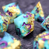 A close-up of several teal resin polyhedral dice with gold accents scattered on a dark surface.