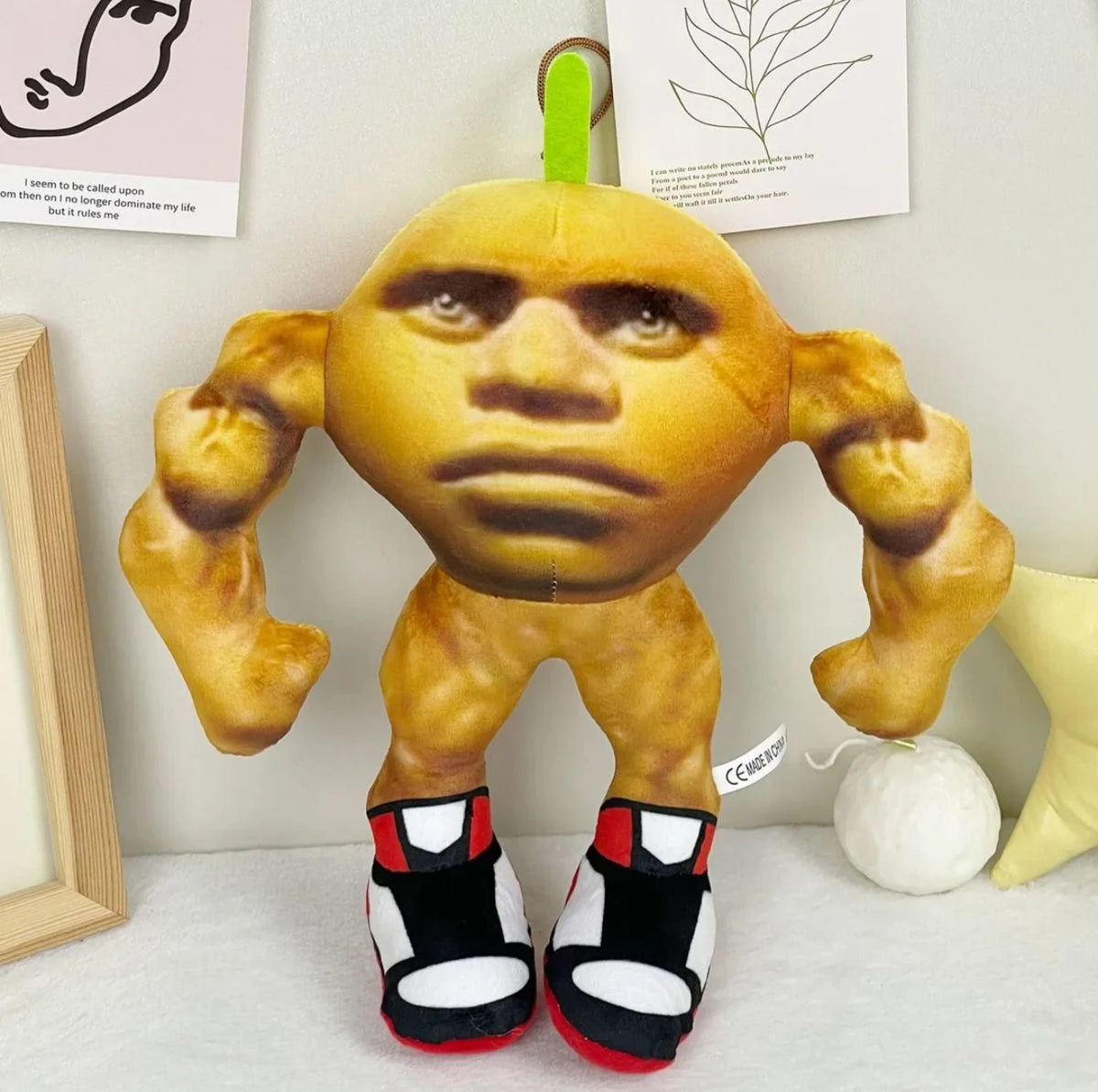 A golden-brown plush toy shaped like a shark head with large eyes and muscular arms, displayed against a white background.