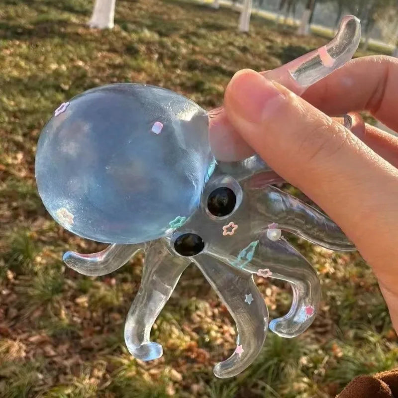 A hand holds a clear, squishy ocean octopus fidget toy with starfish details against a grassy outdoor background.