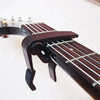 A close-up view of a dark wood guitar capo set with picks and holder on a fretboard.