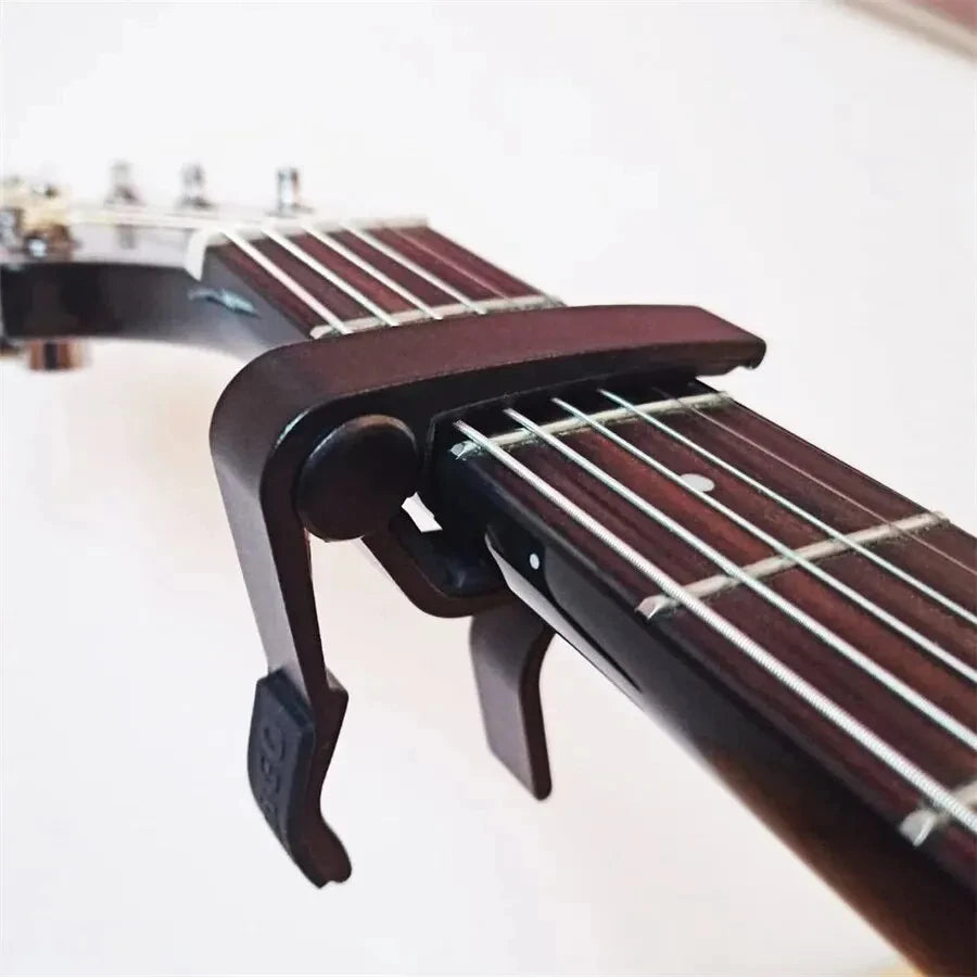 A close-up view of a dark wood guitar capo set with picks and holder on a fretboard.