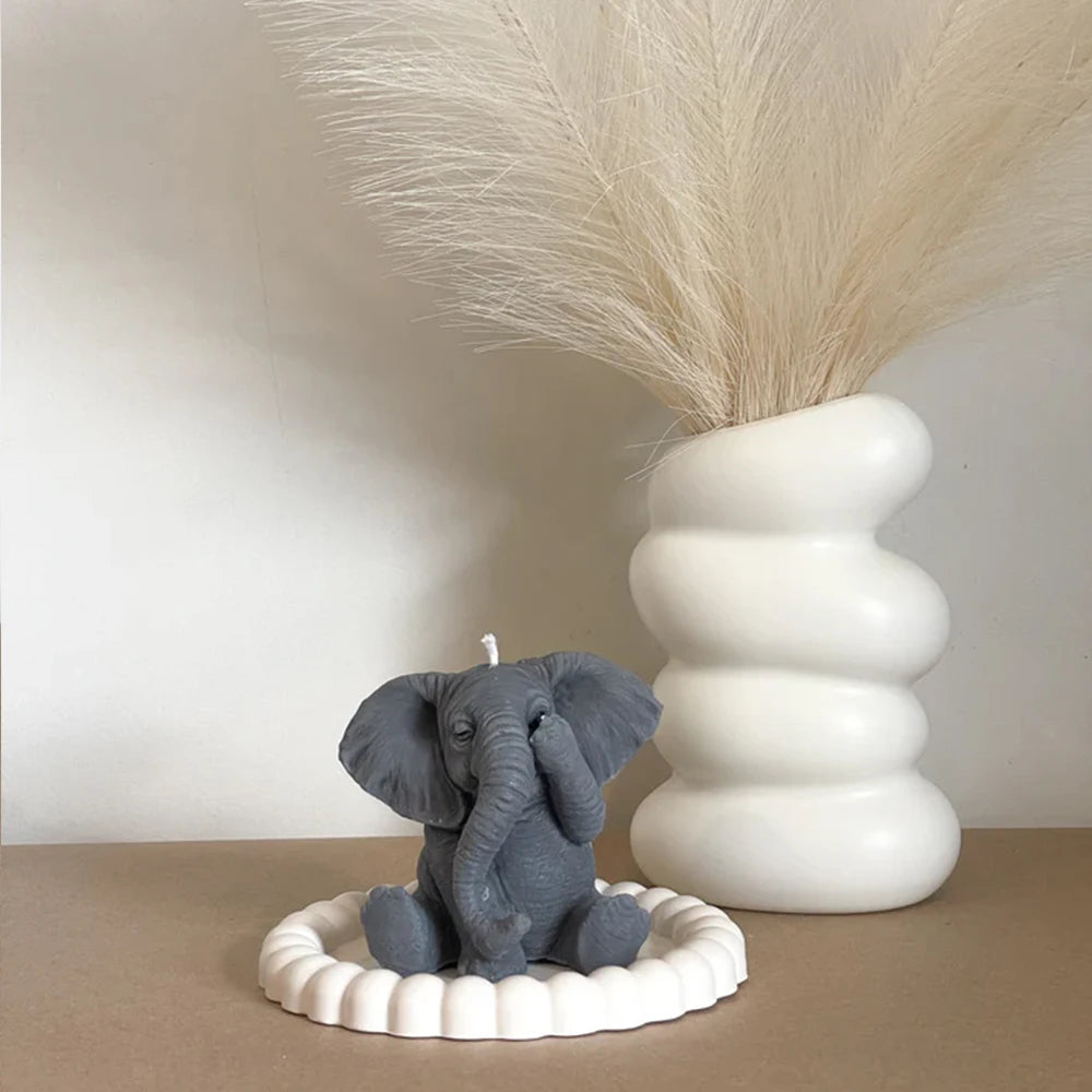 A gray elephant sculpture sits on a white dish next to a large dried feather arrangement.