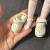 A pair of white fashion slippers designed for 1/6 BJD dolls, shown being held in a hand.