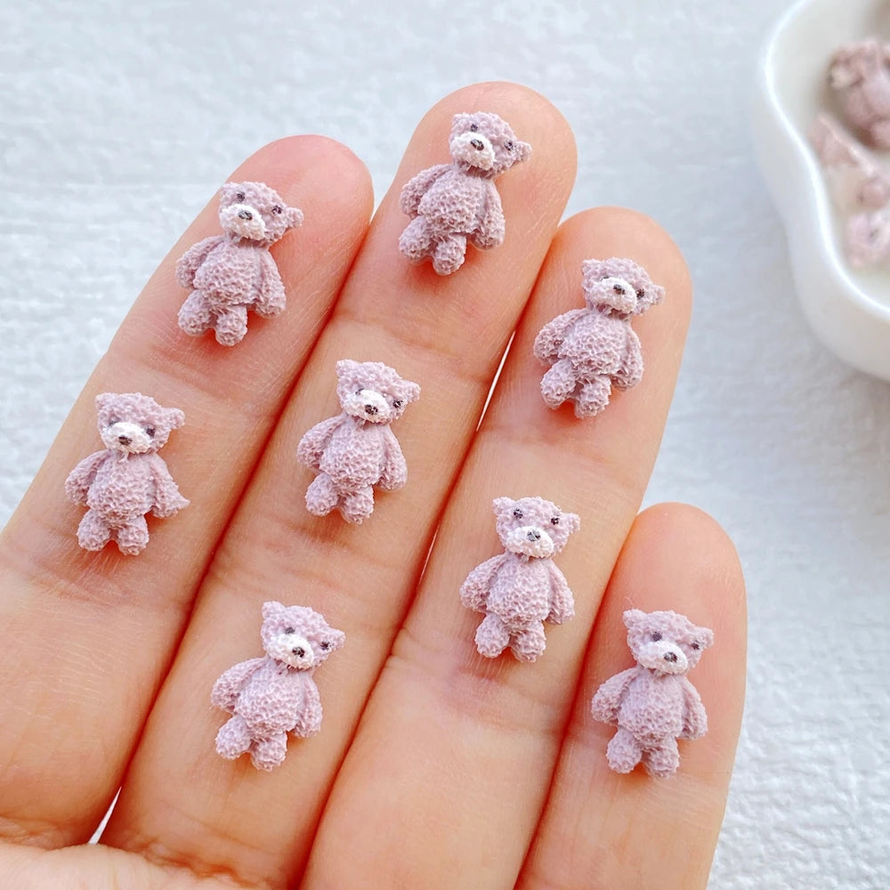Ten fingers display small, pink resin teddy bear charms for DIY crafts
