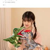 Une jeune fille tient un marionnette dinosaure en peluche avec des écailles vertes et grises.