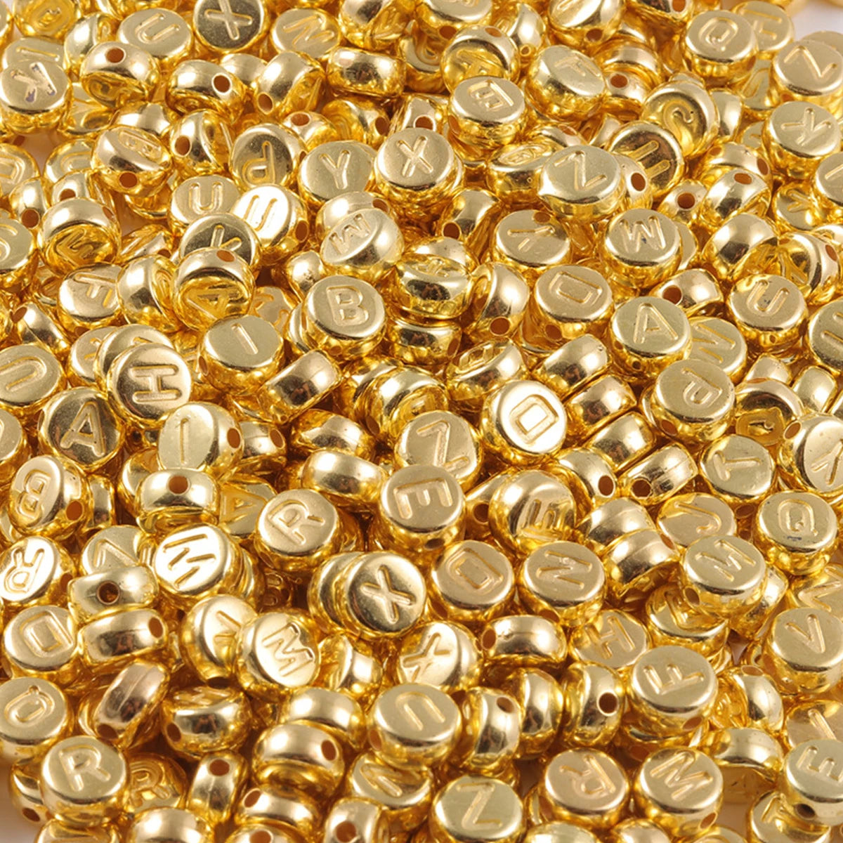 A close-up view of a pile of round, gold-colored acrylic alphabet beads for jewelry making.